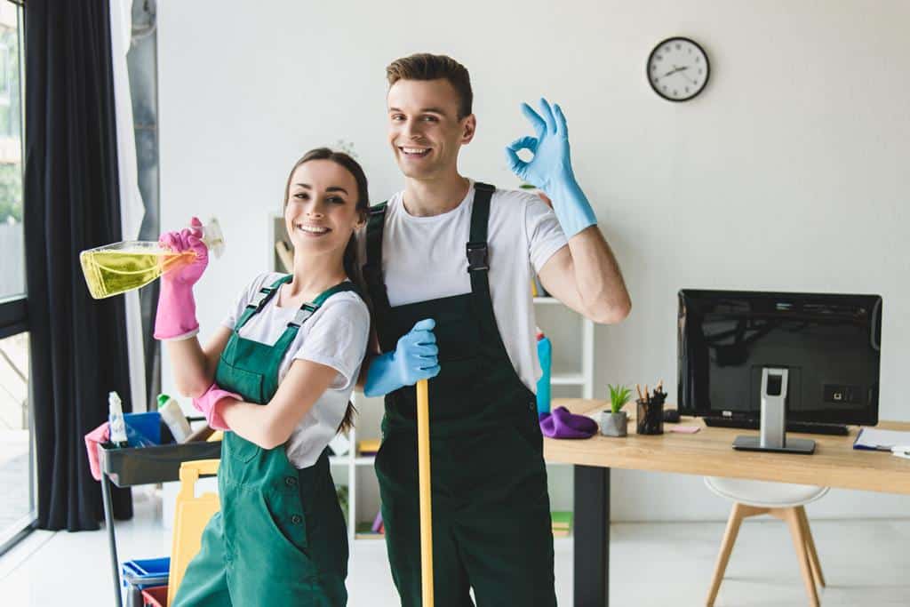 happy young cleaning company workers holding cleaning equipment showing sign